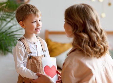 Oğlu, yatak odasında mutlu anneyi tebrik ederken el yapımı tebrik kartı veriyor.