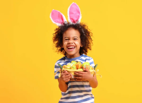 可爱的非洲裔美国小男孩 留着卷曲的头发 条纹T恤 头上戴着兔子耳朵 一边拿着复活节篮子 一边笑 — 图库照片