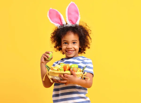 可爱的非洲裔美国小男孩 留着卷曲的头发 条纹T恤 头上戴着兔子耳朵 一边拿着复活节篮子 一边笑 — 图库照片