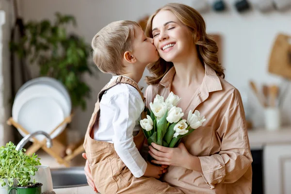 楽観的な家族 チューリップの花束を持つ母親笑顔と家での休日のお祝いの母の日の間に幸せな息子とキス — ストック写真