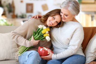 Mutlu genç kız ve yaşlı anne rahat koltukta otururken gülümsüyor ve Uluslararası Kadınlar Günü boyunca hediyeler veriyor ve sarılıyorlar.