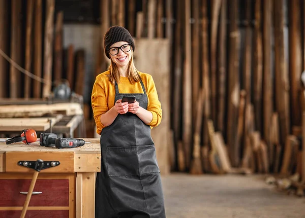 Glad Positiv Ung Kvinnlig Träarbetare Förkläde Meddelanden Mobiltelefon Och Ler — Stockfoto