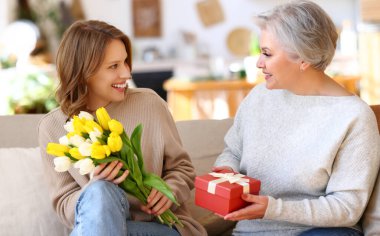 Mutlu genç kız ve yaşlı anne rahat koltukta otururken gülümsüyor ve Uluslararası Kadınlar Günü boyunca birbirlerine hediyeler veriyorlar.