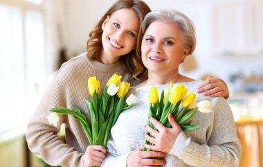 Anneler Günü kutlamaları sırasında evde taze lalelerle dikilmiş, gülümseyen ve kucaklaşan büyük annesi olan pozitif bir genç kız.