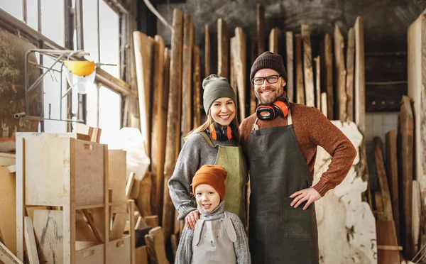 快乐的家庭 穿着围裙的小男孩和笑着的父母站在专业木工车间里看着相机 — 图库照片
