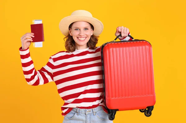流行のカジュアルな服や帽子で楽しい若い女性黄色の背景に対する夏の旅の準備ができて旅行のためのスーツケースや文書を示す — ストック写真