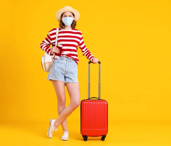 全身の認識できない若い女性旅行者でカジュアル服と顔マスクスタンディングで黄色に対してスーツケースとカメラを見て — ストック写真