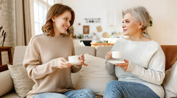 若いです陽気若いです女性ともに中年お母さん飲むお茶とチャットフレンドリーで一緒に座っていますソファにホーム — ストック写真