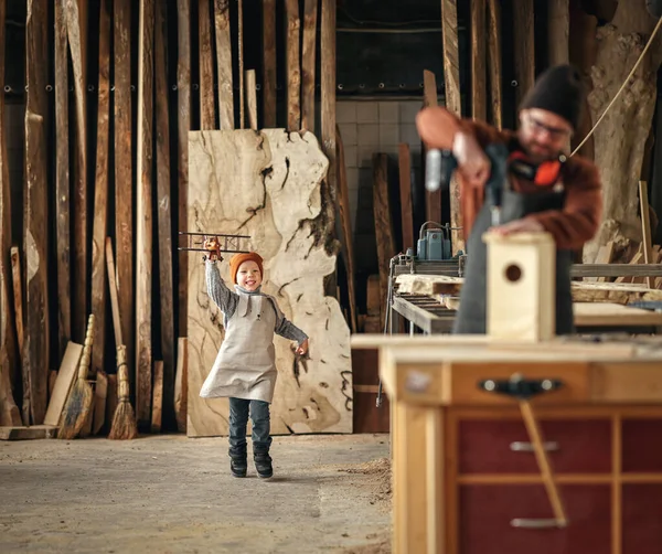 兴奋的小男孩在围裙上花时间和爸爸一起在木工车间里做木制鸟屋 — 图库照片