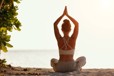 Gün batımında okyanus kıyısında poz veren barışçıl, sağlıklı bir kadın.