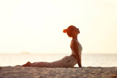 Gün batımında okyanus kıyısında poz veren barışçıl, sağlıklı bir kadın.
