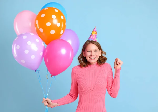 快乐的女人 拿着一束五颜六色的气球紧握着拳头 微笑着看着相机 在蓝色背景下庆祝生日 — 图库照片