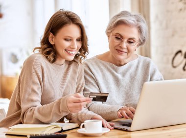 Genç kız, evde internetten alışveriş yaparken gülümsüyor ve kredi kartıyla yaşlı bayana bakıyor.