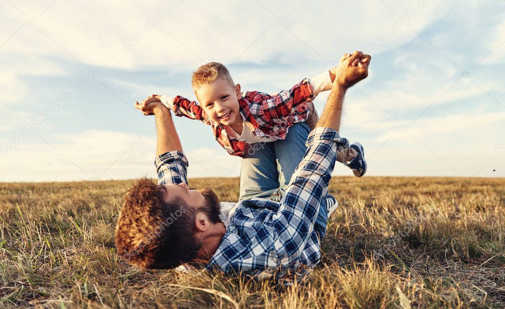 Happy family: father   lying on  autumn grass and throwing up cheerful little son in nature  