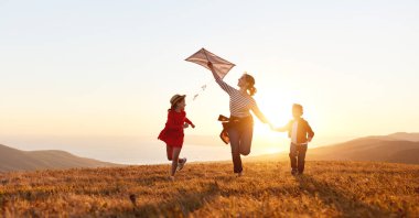 Mutlu aile anne ve çocukları gün batımında doğaya bir uçurtma fırlatırlar.