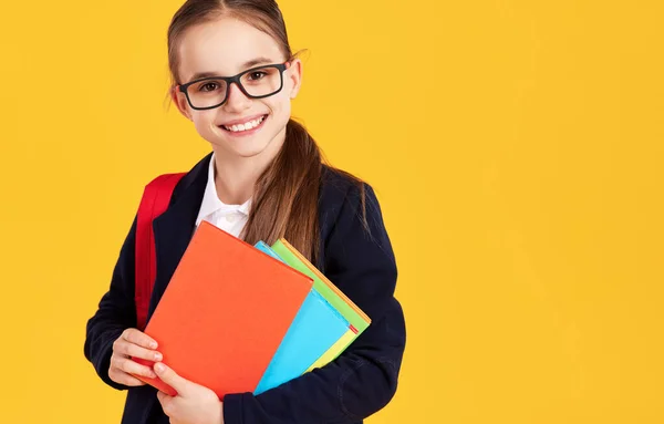 可愛いですスマート女の子でガラス笑顔と見ますカメラともに教科書とともに学校研究中に黄色の背景 — ストック写真