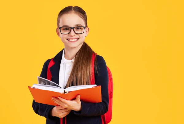在黄色背景的学校学习期间 戴眼镜笑着看着带着课本的相机的漂亮聪明女孩 — 图库照片