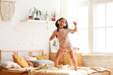 Küçük yıldız. Evde yatağında şarkı söyleyip dans eden sevimli, mutlu, pijama giymiş, saç fırçası takmış, ünlü bir şarkıcıymış gibi davranan küçük kız.
