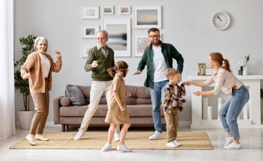 Büyük mutlu aile büyükbabaları, baba, anne ve iki kardeş dans ediyor ve yeni evdeki oturma odasında eğleniyorlar. Hafta sonu birlikte vakit geçiriyorlar. Eğlenceli aktiviteler.