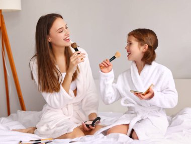 Neşeli genç anne ve mikrofon gibi fırçası olan tatlı küçük kız makyaj sırasında yatakta dinlenirken şarkı söylüyor.