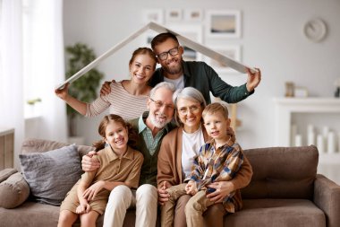 Büyük mutlu bir aile, büyükanne, anne, küçük çocukları olan baba yeni bir eve taşınmayı kutluyor kağıt çatının altında otobüste oturuyor ve kameraya gülümsüyor. İpotek kredisi kavramı