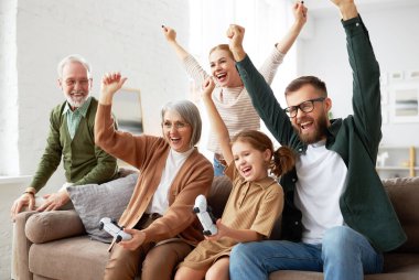 Çılgın hafta sonu. Heyecanlı büyük bir aile, büyükanne ve büyükbaba ve küçük çocuklar oturma odasında kanepede oturup eğlenirken ve birlikte vakit geçirirken oyun oynuyorlar.