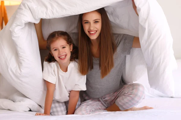 乐观的家庭 年轻的母亲和女儿在舒适的床上坐在温暖的被褥下 微笑着看着相机 — 图库照片