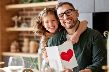 Mutlu aile babasının portresi heyecanlı bir çocuk kızıyla birlikte evde babalar gününü kutlarken kameraya gülümsüyor. Küçük kız, babaya ev yapımı tebrik kartı yolluyor.