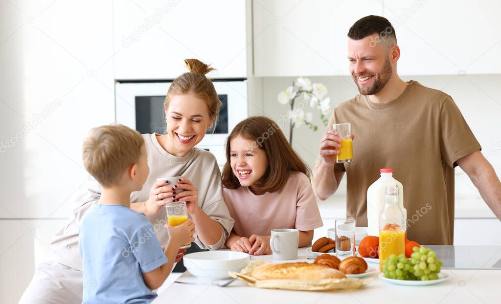 Family morning at home. Happy father, mother and two kids brother and sister enjoying time together while having healthy breakfast, drinking tea, orange juice and eating cookies in kitchen