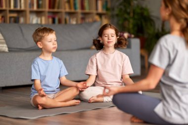 İki sakin çocuk nilüfer çiçekli erkek ve kız kardeş anne ile evde otururken gözlerini kapatıp meditasyon yapıyorlar. Anne çocuklara nasıl meditasyon yapılacağını öğretiyor.