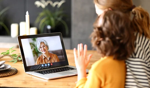 Aile video görüşmesi. Anne ve kızının büyükannesiyle konuştuğu ve dizüstü bilgisayarda el salladığı, evde boş zaman geçirdiği, bilgisayar ekranına seçici bir şekilde odaklandığı arka plan görüntüsü