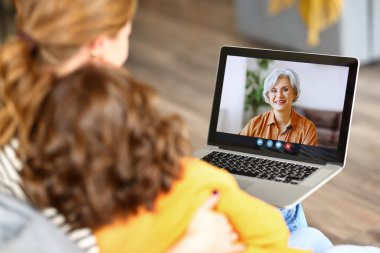 Aile video görüşmesi. Anne ve kızının dizüstü bilgisayarla konuşurken, evde boş vakitlerinde bilgisayar ekranına odaklandığı arka plan görüntüsü.