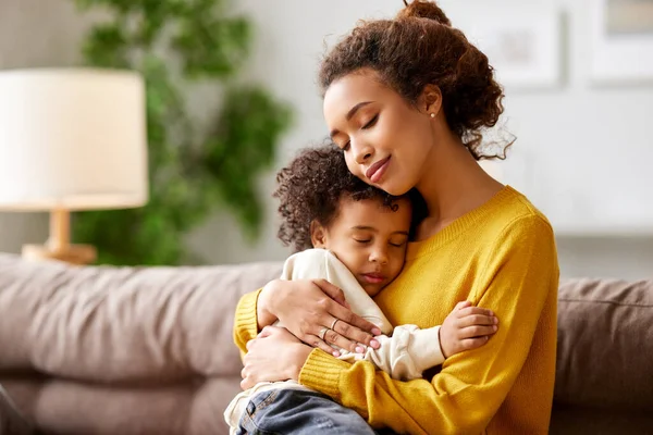 Happy afro american family at home. Young beautiful loving mom with closed eyes embracing cute little kid son while sitting on sofa in living room at home. Mother expressing love to small child