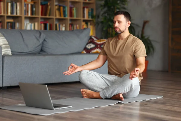 年轻宁静的男性穿着运动服 闭着眼睛沉思 做呼吸练习 同时在家里的笔记本电脑上开设瑜伽课 全身而退 留意人类在检疫期间的活动 — 图库照片