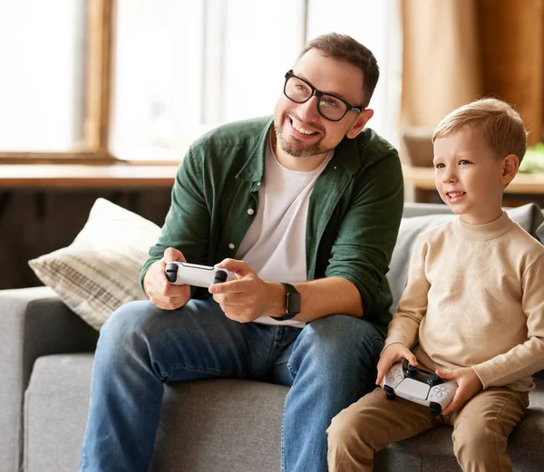 Gerçek rekabet. Mutlu aile, erkek baba ve heyecanlı çocuk evlerinde boş vakitlerini birlikte geçirirken video konsolu oyunları oynuyorlar, evdeki oturma odasında kanepede oturuyorlar.
