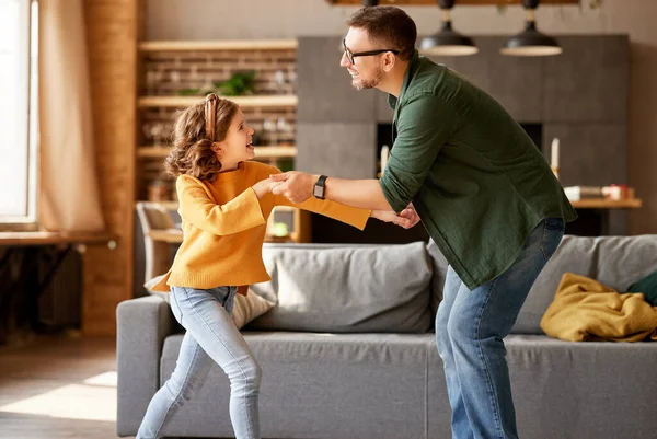 パパと楽しんでる カジュアルウェアダンスでかわいい興奮した女の子と若い遊び心のある父親の完全な足は 自宅のリビングルームに立っている間に一緒に踊っています 家族のレジャー活動 — ストック写真