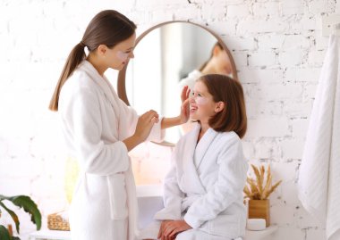 Genç bir kadın banyoda cilt bakımı sırasında mutlu bir reşit olmayan kızın yüzüne bant yapıştırıyor.