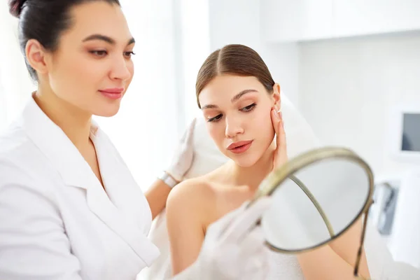 Jovem Satisfeita Olhando Para Espelho Rosto Tocante Após Tratamento Cosmetologia — Fotografia de Stock