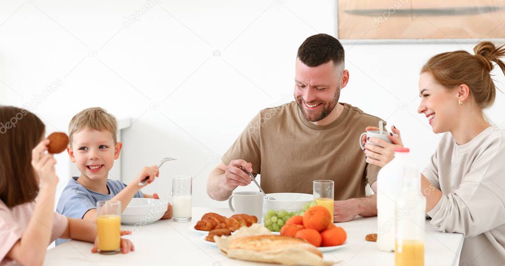 Family morning at home. Happy father, mother and two kids brother and sister enjoying time together while having healthy breakfast, drinking tea, orange juice and eating cookies in kitchen