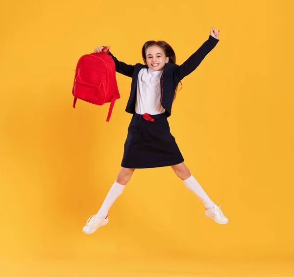 全身上下都是身穿黑色校服 戴着眼镜 快乐的学龄前女学生 背对着黄色背景跳得很高 — 图库照片