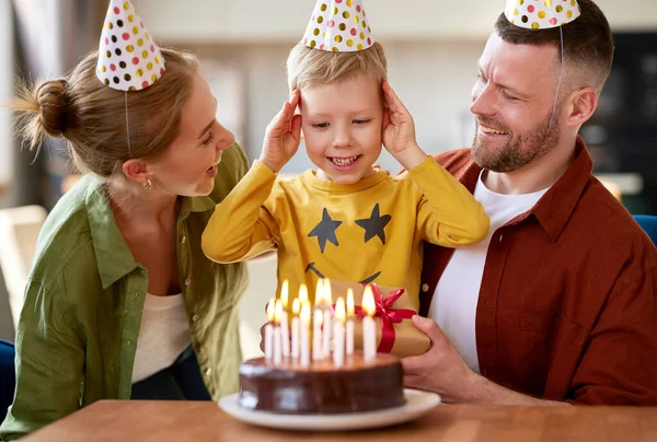小さな男の子の息子は 若い愛情のある両親と誕生日を祝いながら ケーキの上にろうそくを吹きに行きます お祝いを受けながら 興奮した子供は腕を上げて笑顔と家族からプレゼント — ストック写真