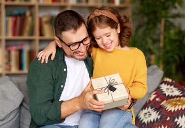 Sevgili babam için Noel sürprizi. Şirin küçük kız Noel 'de babasından hediye paketi alırken babasının dizlerinin üstüne çöküp ona bakıyor ve gülümsüyor. Aile kutlama konsepti