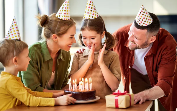 興奮した女の子はチョコレートケーキの上にろうそくを吹き 家で幸せな家族と彼女の誕生日を祝いながら願いを作ります パーティー帽子の正の両親お祝いの娘 — ストック写真