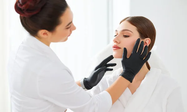 Crop Cosmetologist Zwarte Handschoenen Onderzoeken Gezichtshuid Van Jonge Vrouwelijke Client — Stockfoto