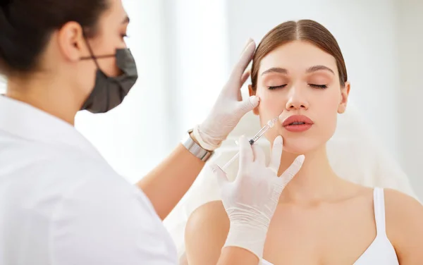 美容クリニックで美容治療中に若い女性のクライアントの顔に注射を適用保護マスクや手袋のプロの美容師 — ストック写真