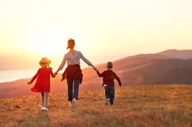 Mutlu aile manzarası: anne ve iki çocuk gün batımında dışarı koşuyorlar.