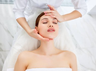 Güzellik uzmanı ya da masör genç bir kadın için miyofasyal ya da buktal kafa ve yüz masajı yapıyor. Kadın hasta spa merkezinde yatıyor, yaşlanmayı önleyen güzellik tedavisi görüyor. Cilt tazeleme kavramı