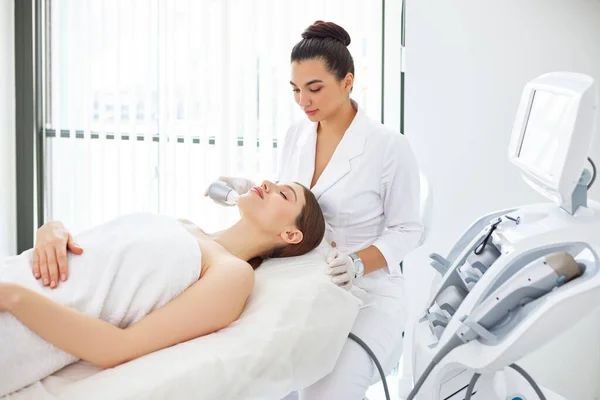 Relaxed young female patient receiving ultrasound face lifting during rejuvenation procedure in beauty clinic