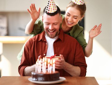 Genç, pozitif bir eş kocaya sürpriz yapıyor. Elinde hediye kutusu olan heyecanlı bir adam. Mutfakta pasta yerken çok mutlu. Parti şapkalı bir çift evde doğum günü kutluyor.