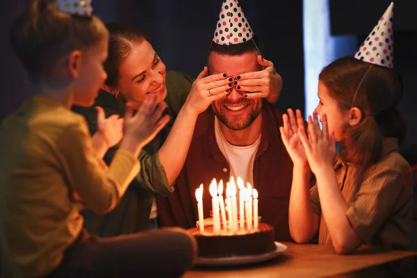 願い事をする時間だ 自宅で誕生日を祝うパーティー帽子をかぶっている子供たちと若い幸せな美しい家族 興奮したお父さんとともにカバーされた目へ行きます打撃キャンドルオンチョコレートケーキ — ストック写真